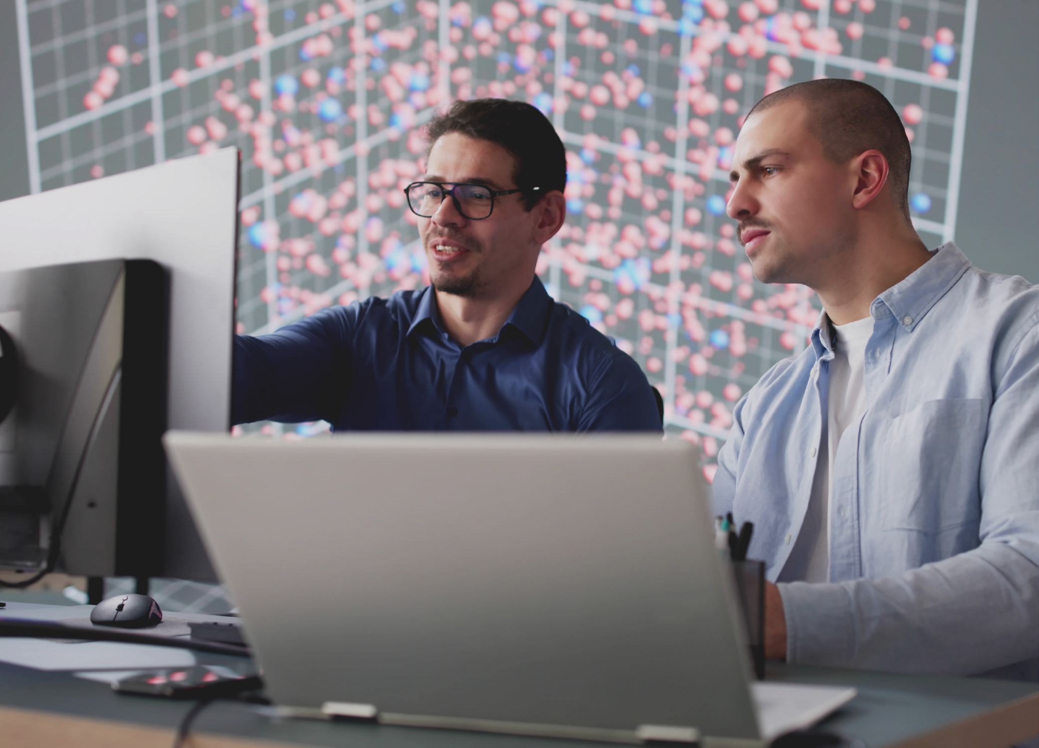 Two men, one on a laptop, one on a desktop, looking at computer screens.