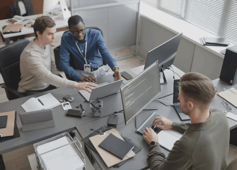 Three employees all working on computers, two of them collaborating on a task.