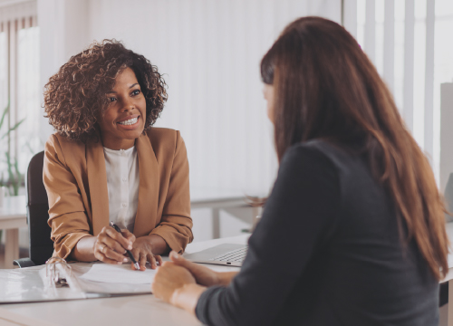 Two women talking over a desk and collaborating on a task.