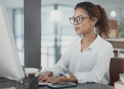 A female employee in glasses working on a computer at her desk.