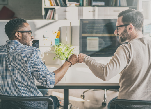 Two male employees giving each other a fist bump as they collaborate.