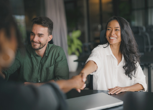 Three employees, one male, one female and one out of focus while two shake hands.