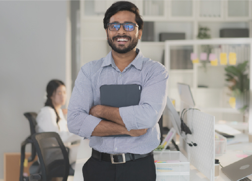 Man smiling while clutching a tablet to his chest in an office setting.