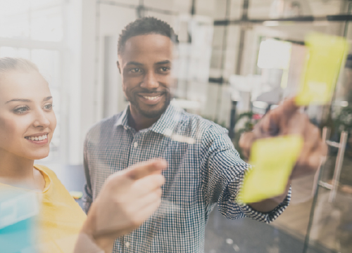 Two employees pointing at Post-It notes on a glass window.