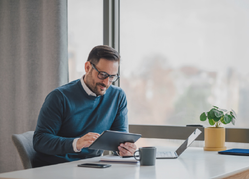 Man in glasses and a sweater holding tablet.