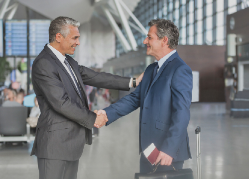 Two men, executives, shaking hands in a business lobby.
