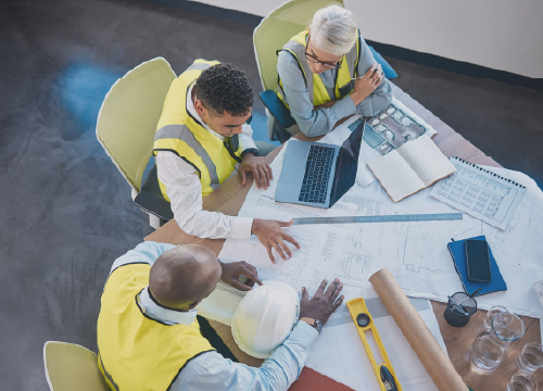 Three people in yellow vests around a table looking at blueprints.