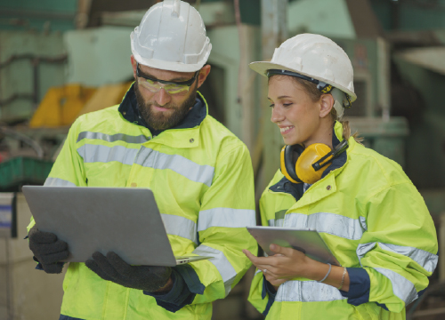 Two workers in yellow jackets and hard hats working in a warehouse.