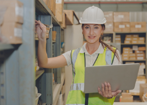 Female warehouse worker holding a laptop and taking inventory and managing supplies.